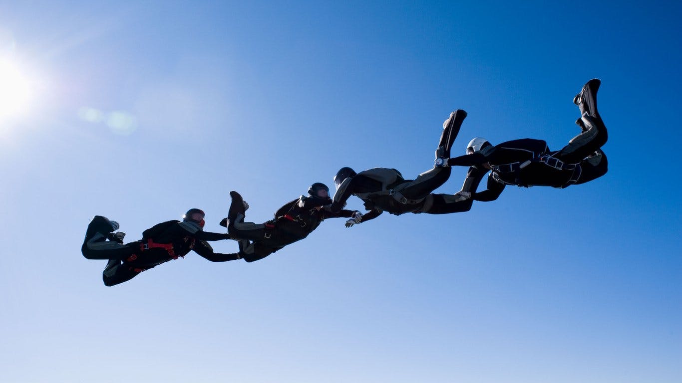 Tre personer som hoppar fallskärm och håller varandra i händerna.